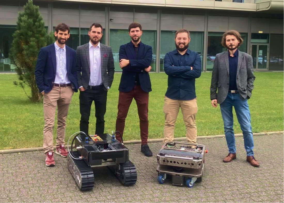 The Hetbot team posing outdoors with two mobile robots in front of a building